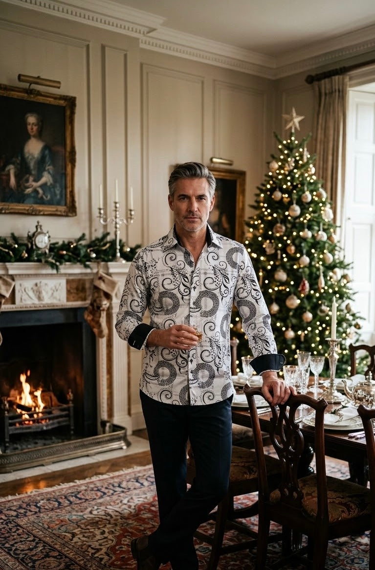 Middle-aged man in patterned white button-up shirt holding a drink beside a decorated Christmas tree and dining table